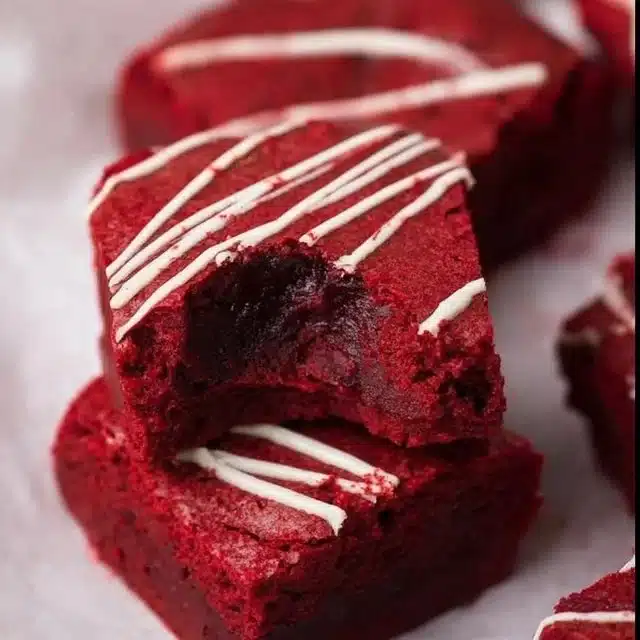 Fudgy red velvet brownies topped with cream cheese frosting on a white plate