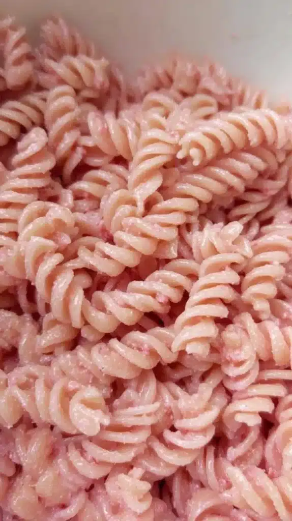 Bowl of pink pasta garnished with fresh herbs and colorful vegetables.