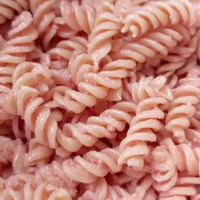 Bowl of pink pasta garnished with fresh herbs and colorful vegetables.